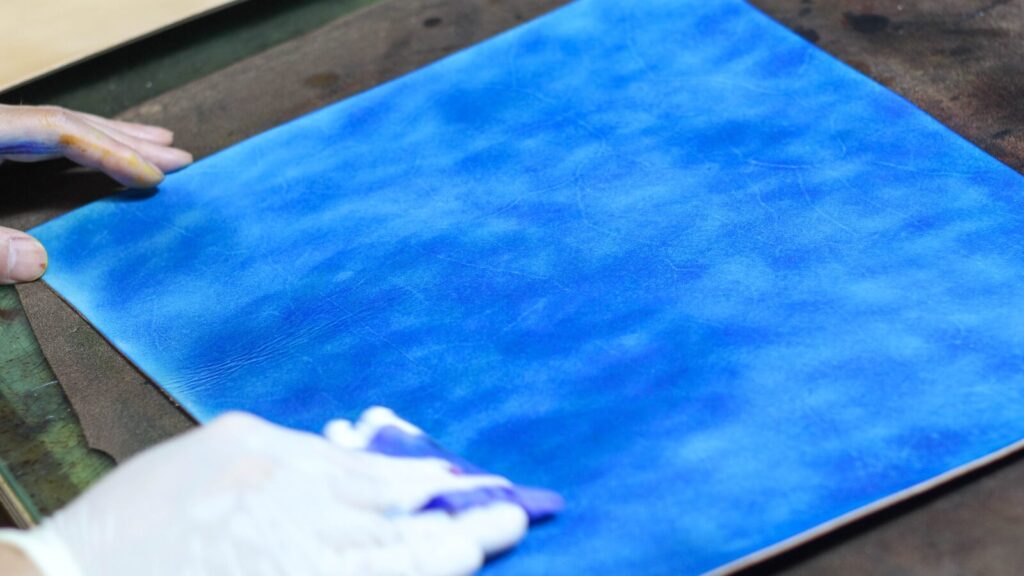 職人が本革ブックカバー「OLIVE」を手染めしている作業風景。アンティーク染めの色の深みが表現されている。