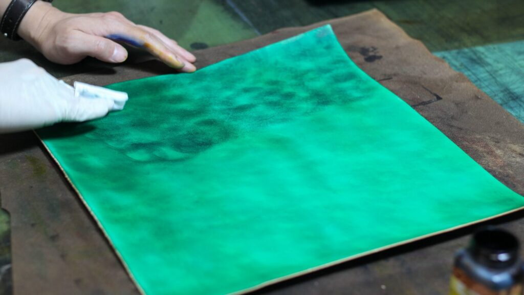 ヌメ革にグリーンの手染めを行う様子。複数の染料で丹念に塗り重ねることで複雑で奥深い模様に仕上がる。