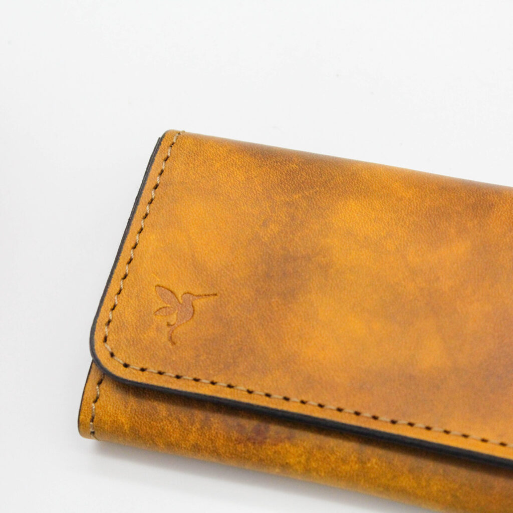 表面にはブランドシンボルのハチドリを刻印。手染めのカラーリングでハチドリの見え方もそれぞれ変わります。